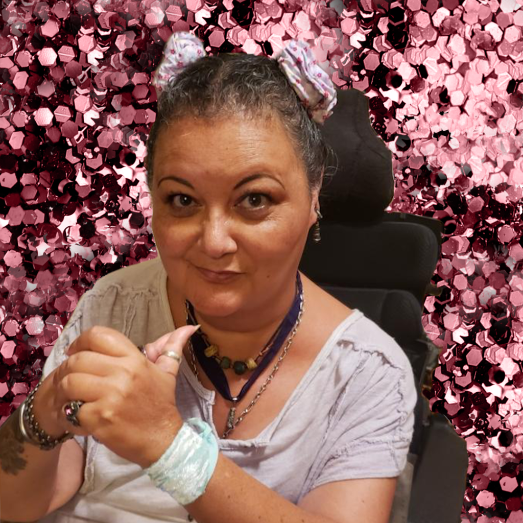 A Japanese-Haitian queer disabled woman with their hair tied in two buns with a slight smile. Behind them are small pink hexagons scattered across the background.