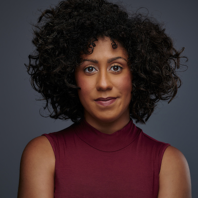 headshot of Afro-Latina woman Jay Woods with curly afro and thin red sweater vest