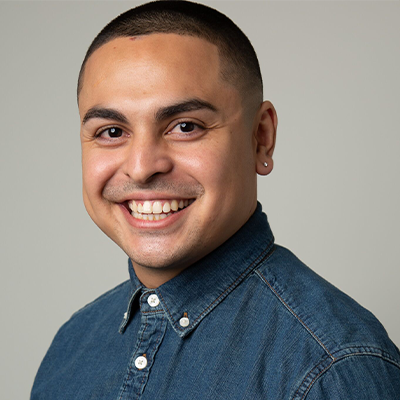 headshot of short-haired Latino man Myles Romo smiling with blue button-up shirt